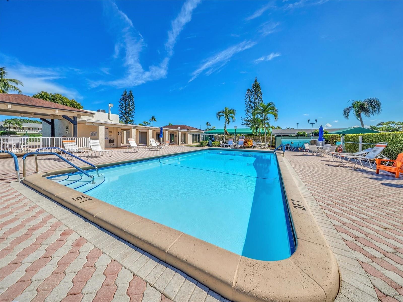 Inground swimming pool with built-in entry steps and metal handrails, surrounded by extensive brick-paver decking and a covered pavilion