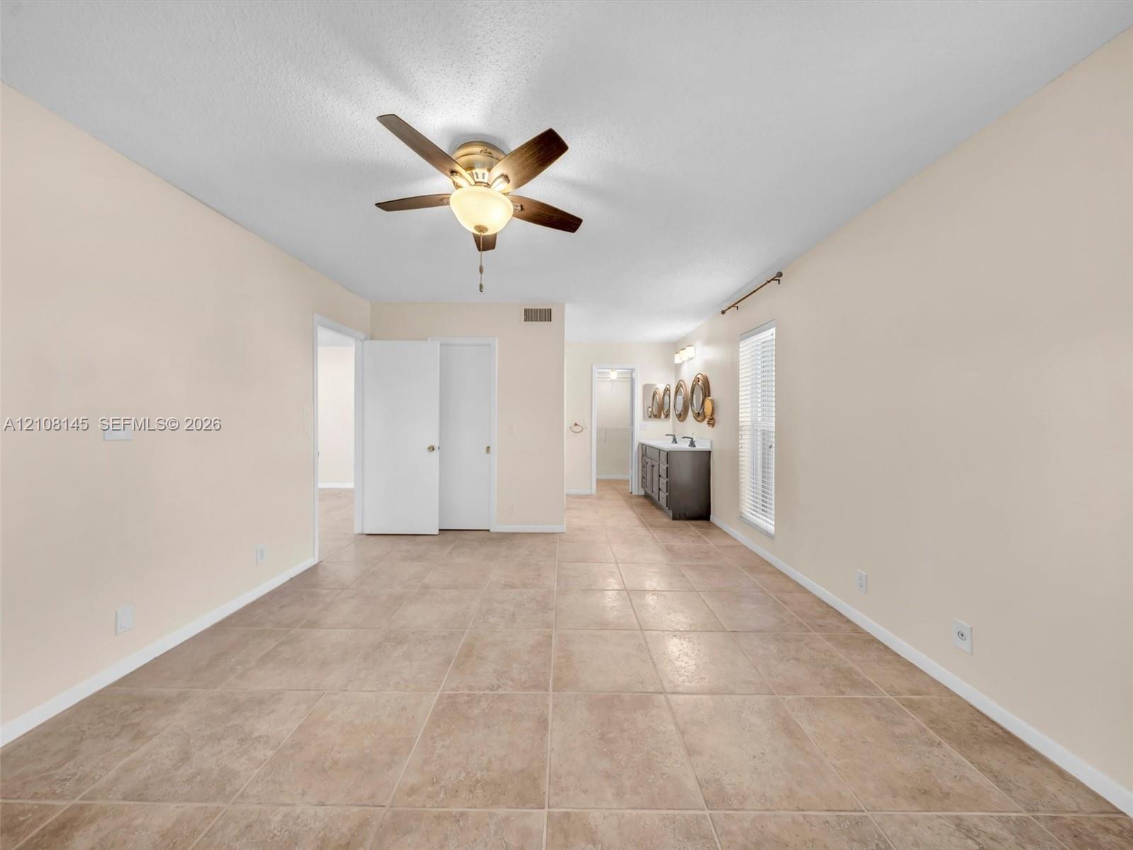Large-format tile flooring, ceiling fan with integrated light fixture, dual-sink vanity with stone-surface countertop, and window blinds