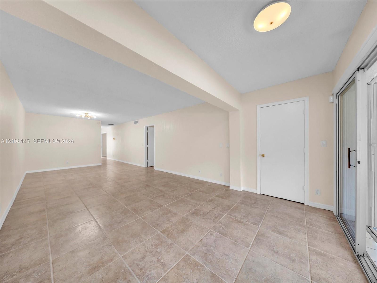 Neutral-toned tile flooring, recessed architectural beam, flush-mount ceiling lighting, and glass sliding door