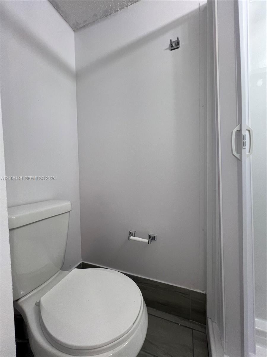 Bathroom featuring a white ceramic toilet, tile flooring, and a shower enclosure with a white frame
