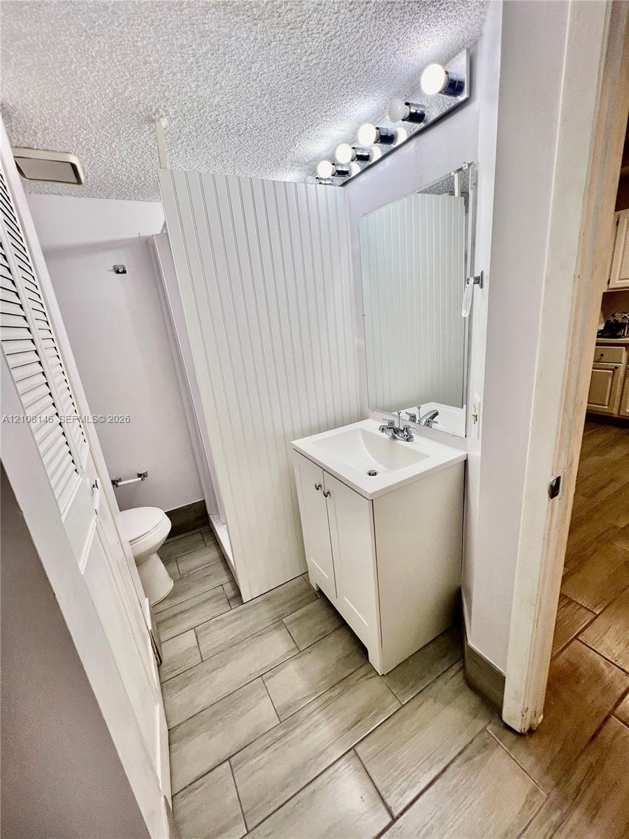 Bathroom featuring wood-finish tile flooring, a white vanity cabinet with an integrated basin, a wall-mounted mirror, and beadboard wall paneling