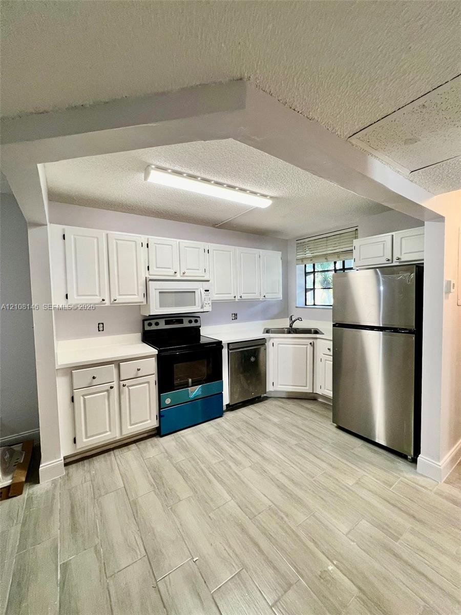 Kitchen featuring white shaker-style cabinetry, stainless steel appliances, solid-surface countertops, and wood-finish tile flooring