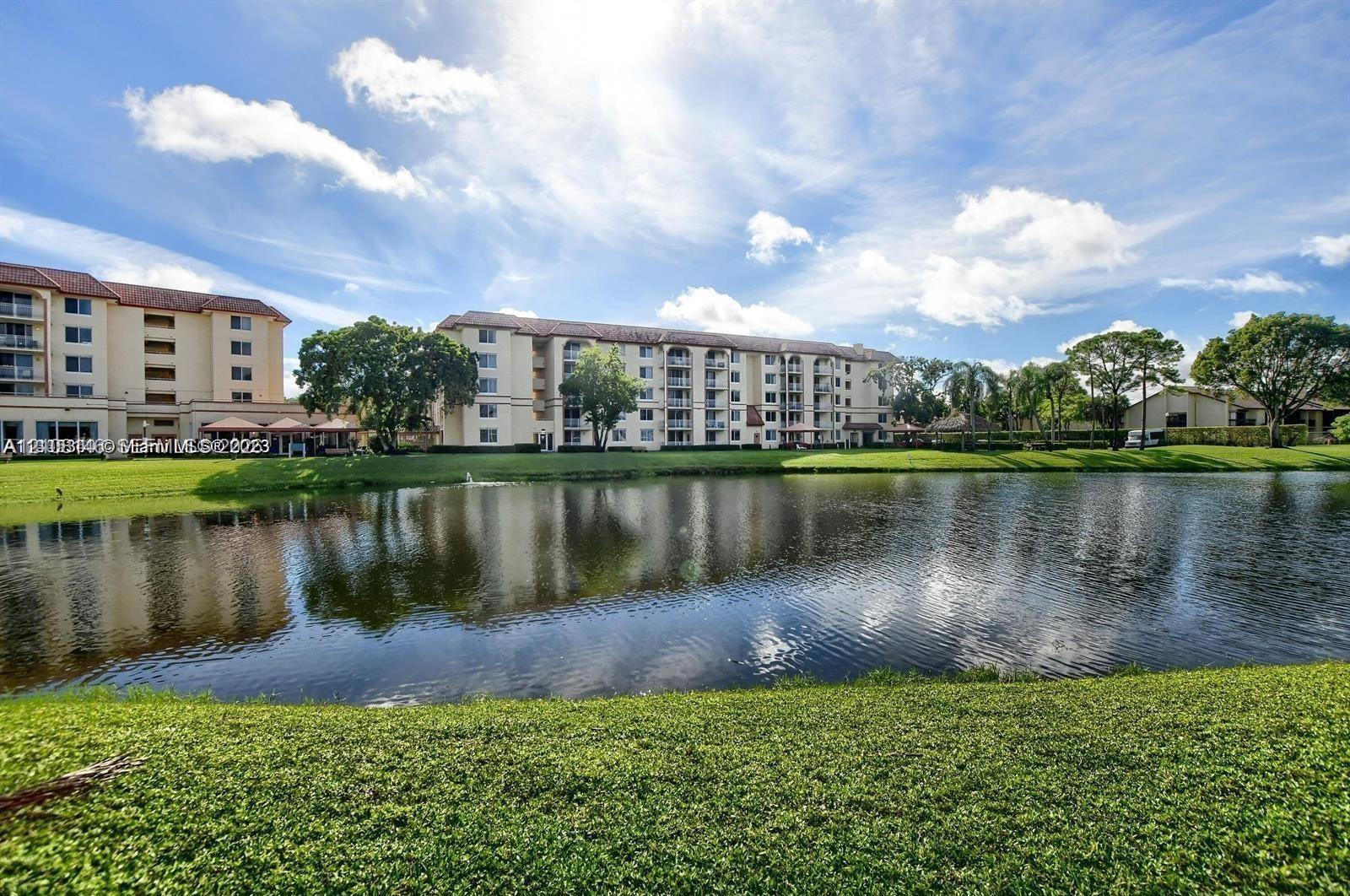Multi-story building with stucco facade and tiled roof, featuring private balconies, mature landscaping, and waterfront grounds