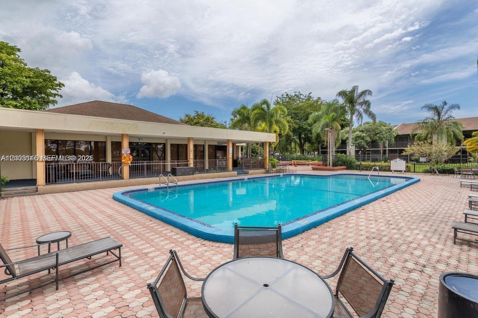 In-ground swimming pool featuring a concrete deck with paver-style finish, covered patio space, and mature perimeter landscaping