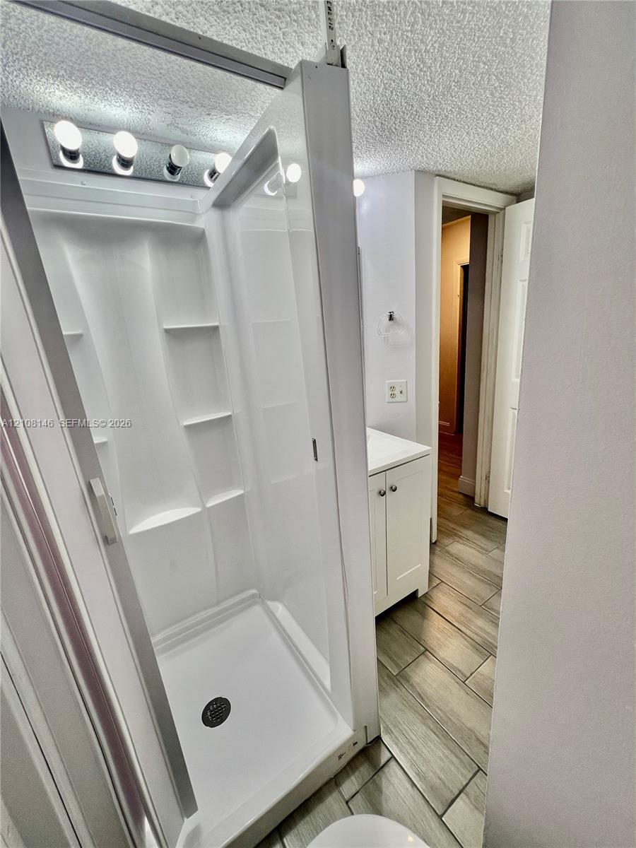 Walk-in shower featuring molded shelving, white vanity with integrated cabinetry, and wood-finish tile flooring