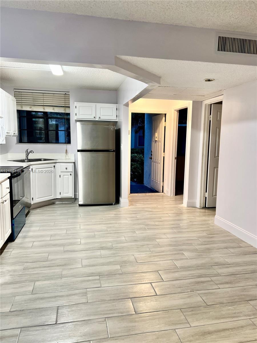 Kitchen featuring wood-finish flooring, white cabinetry, stainless steel appliances, and a solid surface countertop