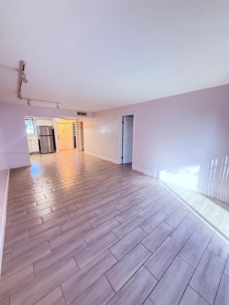 Interior space featuring wood-finish tile flooring, track lighting, and a stainless steel refrigerator