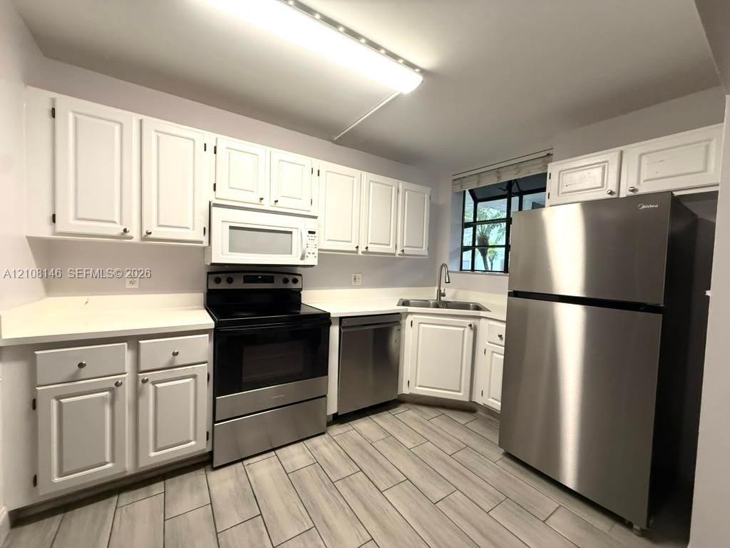Kitchen featuring white cabinetry, stainless steel appliances, solid-surface countertops, and wood-finish tile flooring