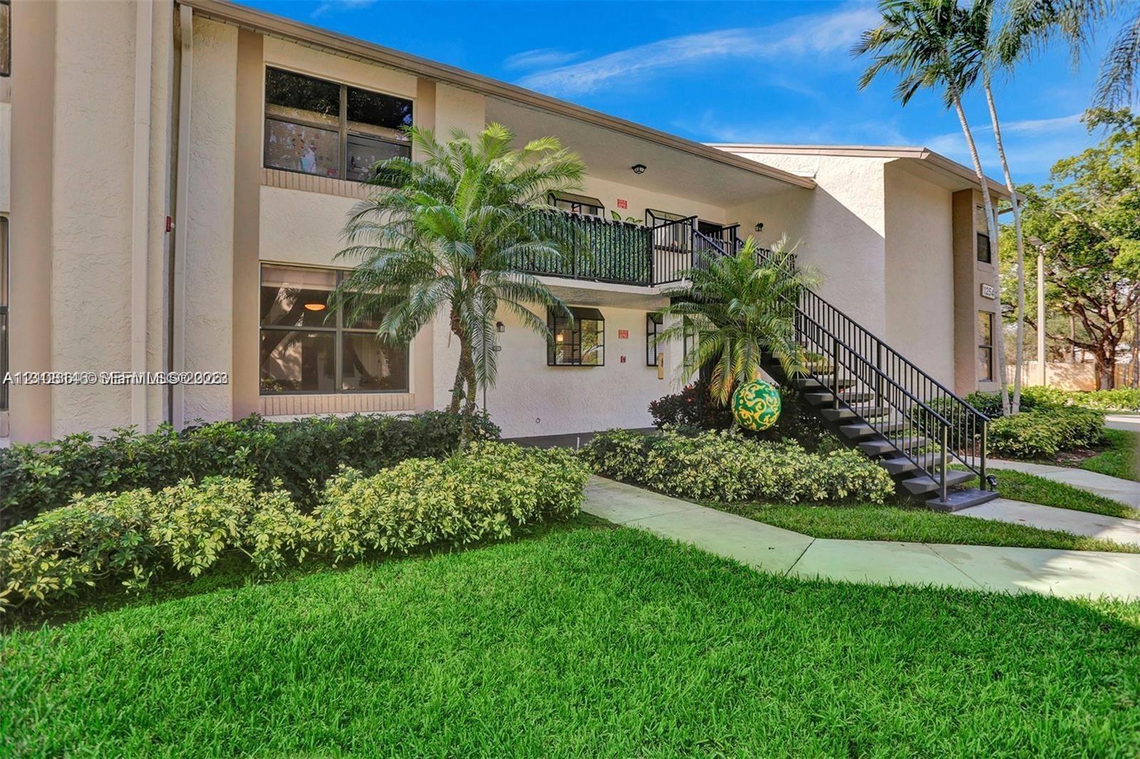 Stucco exterior featuring an elevated balcony, black metal railings, concrete walkway, and mature palm trees