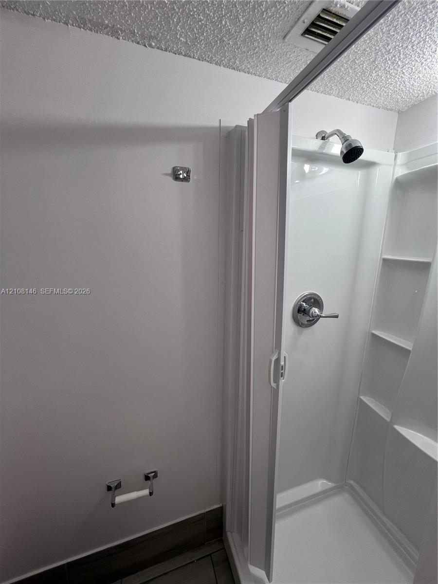 Walk-in shower enclosure with integrated shelving, chrome-finish plumbing fixtures, and tiled flooring