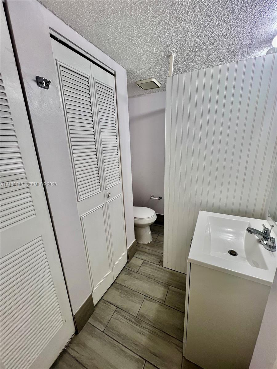 Bathroom featuring wood-finish tile flooring, white beadboard wainscoting, white louvered closet doors, and a pedestal sink with a chrome faucet