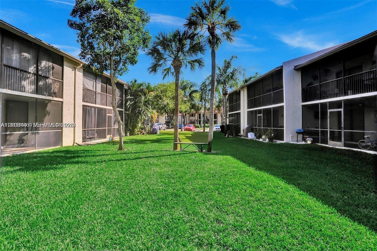 Expansive central courtyard featuring a manicured lawn, mature palm trees, multi-story buildings with screened-in porches, and private balconies