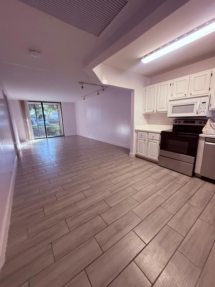 Kitchen featuring white cabinetry, stainless steel appliances, and wood-finish tile flooring, complemented by sliding glass doors and track lighting