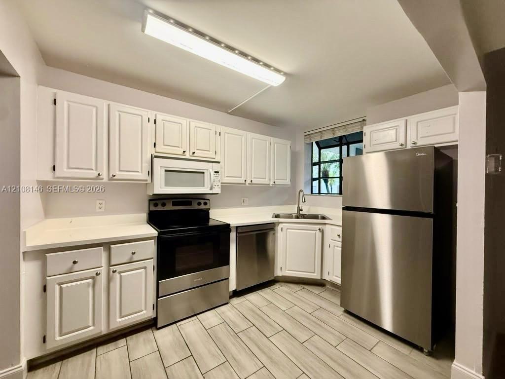 Kitchen featuring white cabinetry, stone-surface countertops, stainless steel appliances, and tile flooring