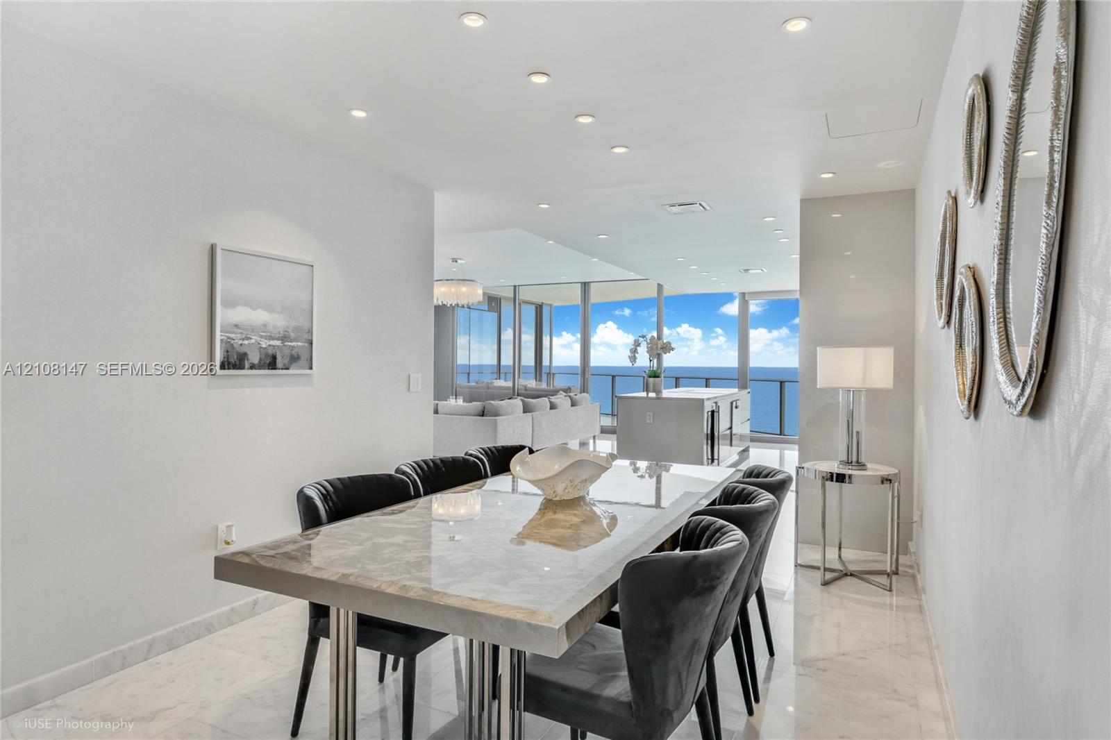 Open-concept floor plan featuring polished stone flooring, recessed ceiling lighting, and floor-to-ceiling glass paneling showcasing an ocean backdrop