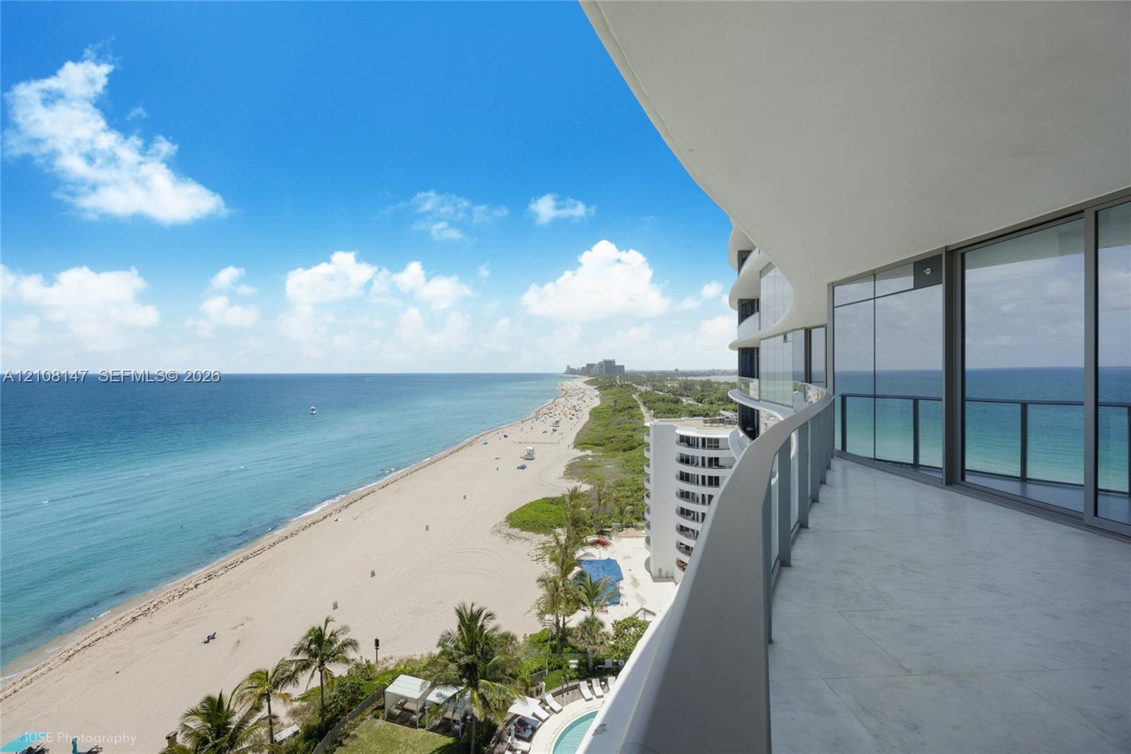 Curved expansive balcony featuring large-format stone flooring, floor-to-ceiling glass paneling, and metal railing