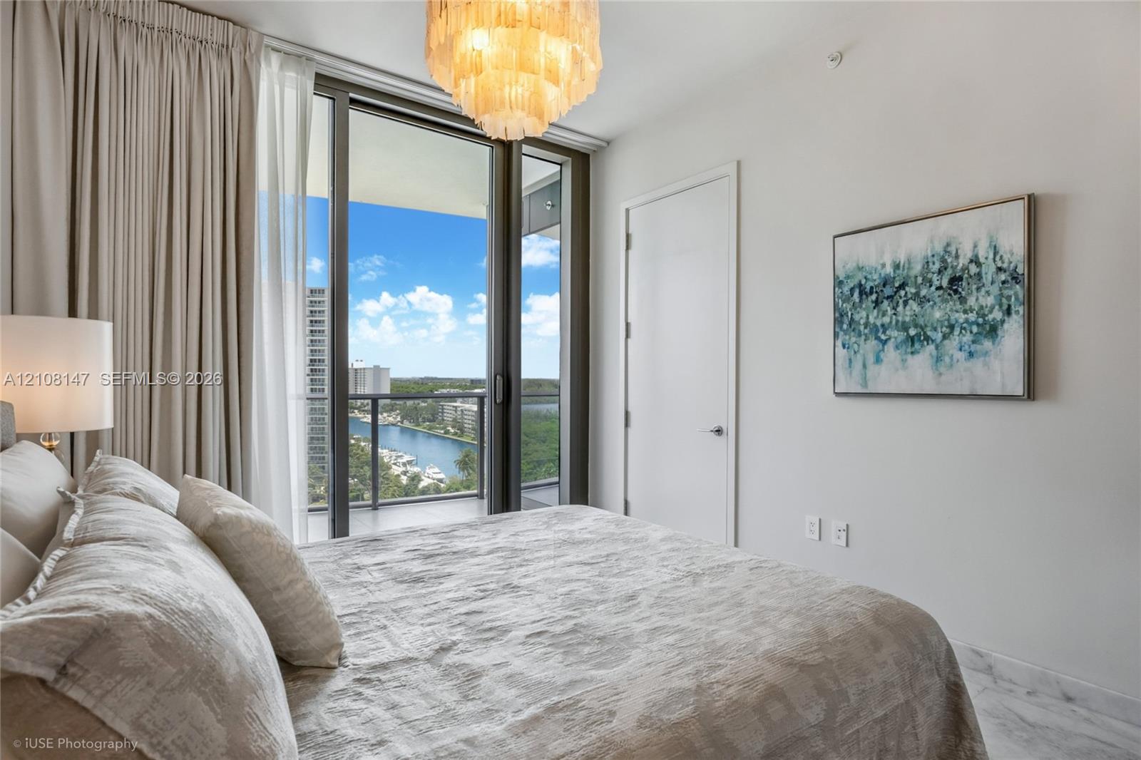Floor-to-ceiling glass sliding doors opening to a balcony, polished stone-finish flooring, and a multi-tiered tiered chandelier