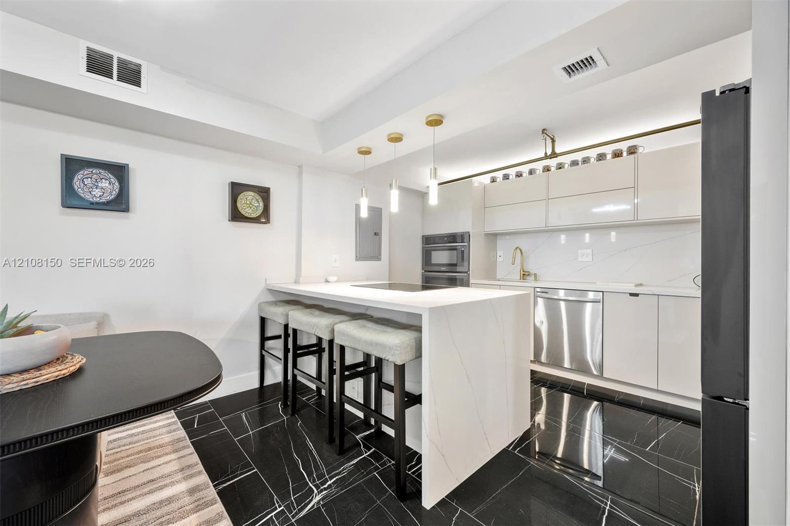 Kitchen featuring an island with a stone-finish waterfall edge, high-gloss cabinetry, stainless steel appliances, pendant lighting, and polished stone-finish flooring Kitchen featuring an island with a stone-finish waterfall edge, high-gloss cabinetry, stainless steel appliances, pendant lighting, and polished stone-finish flooring