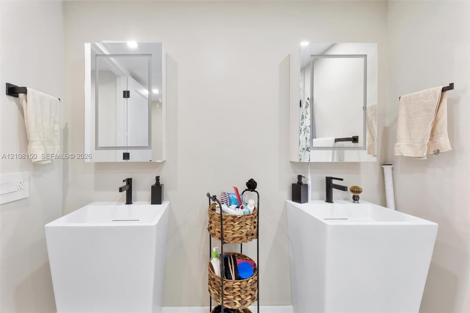 Dual pedestal sinks featuring rectangular basins and matte black faucets, paired with mirrored medicine cabinets and matte black hardware