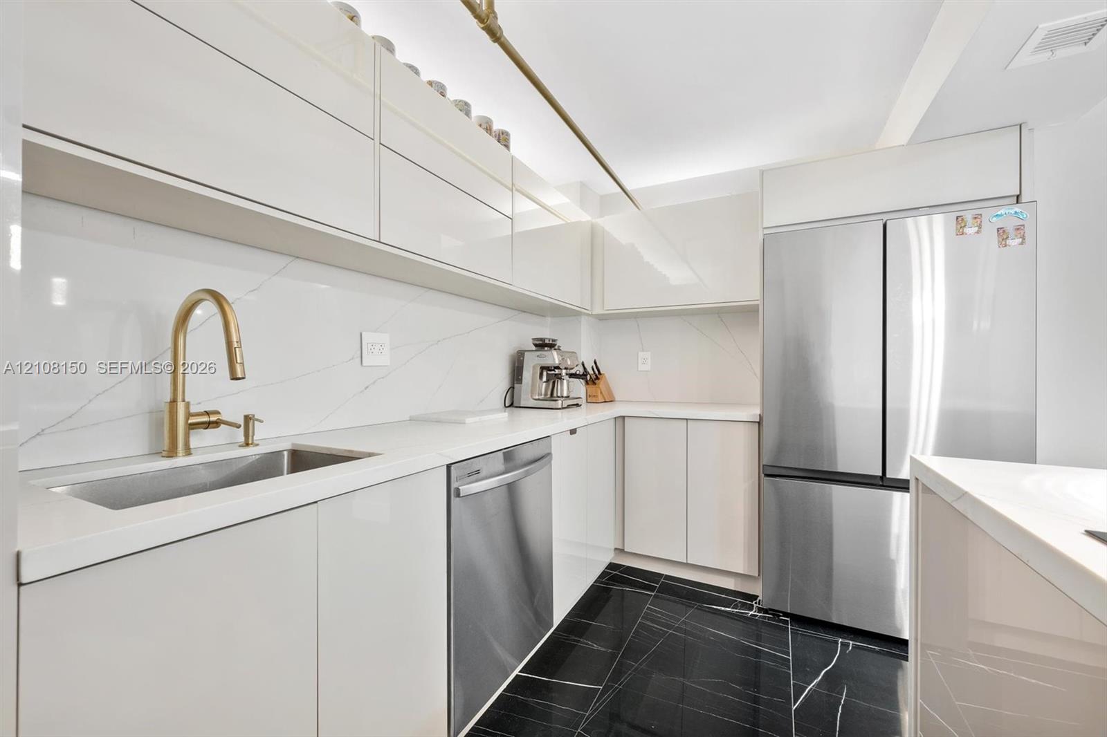Kitchen featuring high-gloss cabinetry, stone-surface countertops, full-height stone backsplash, stainless steel appliances, and dark-toned flooring with light veining