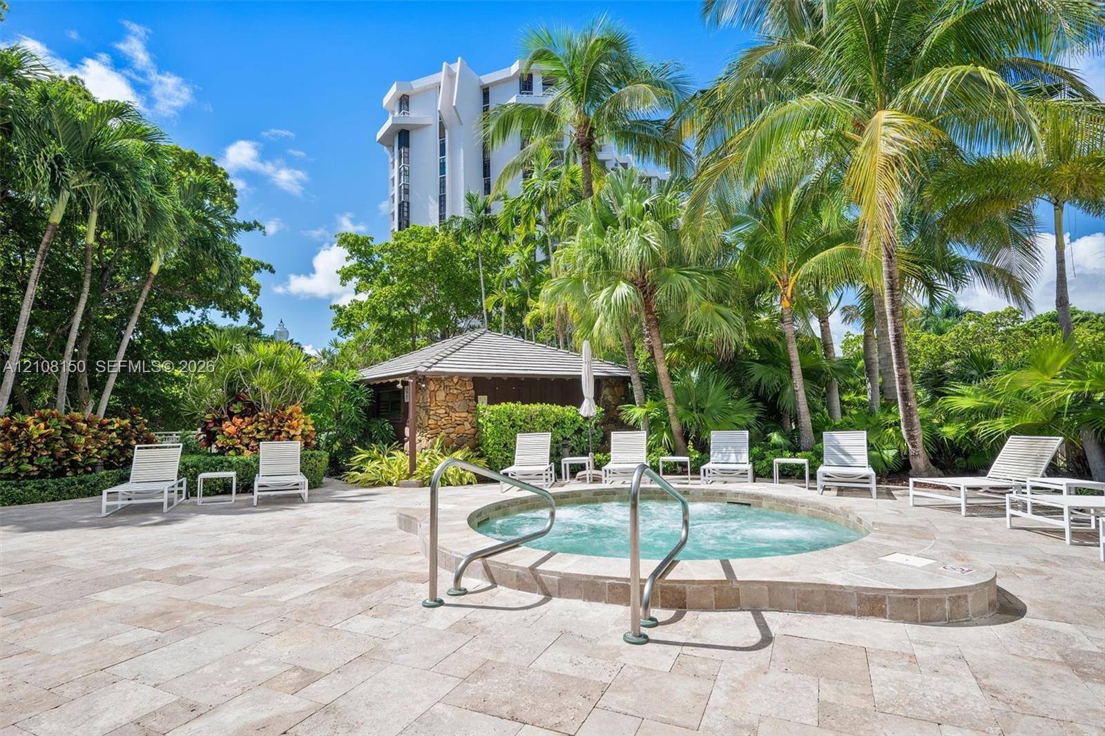 Outdoor spa with stone coping, travertine paver decking, and stone-accented poolside pavilion, surrounded by mature palm trees