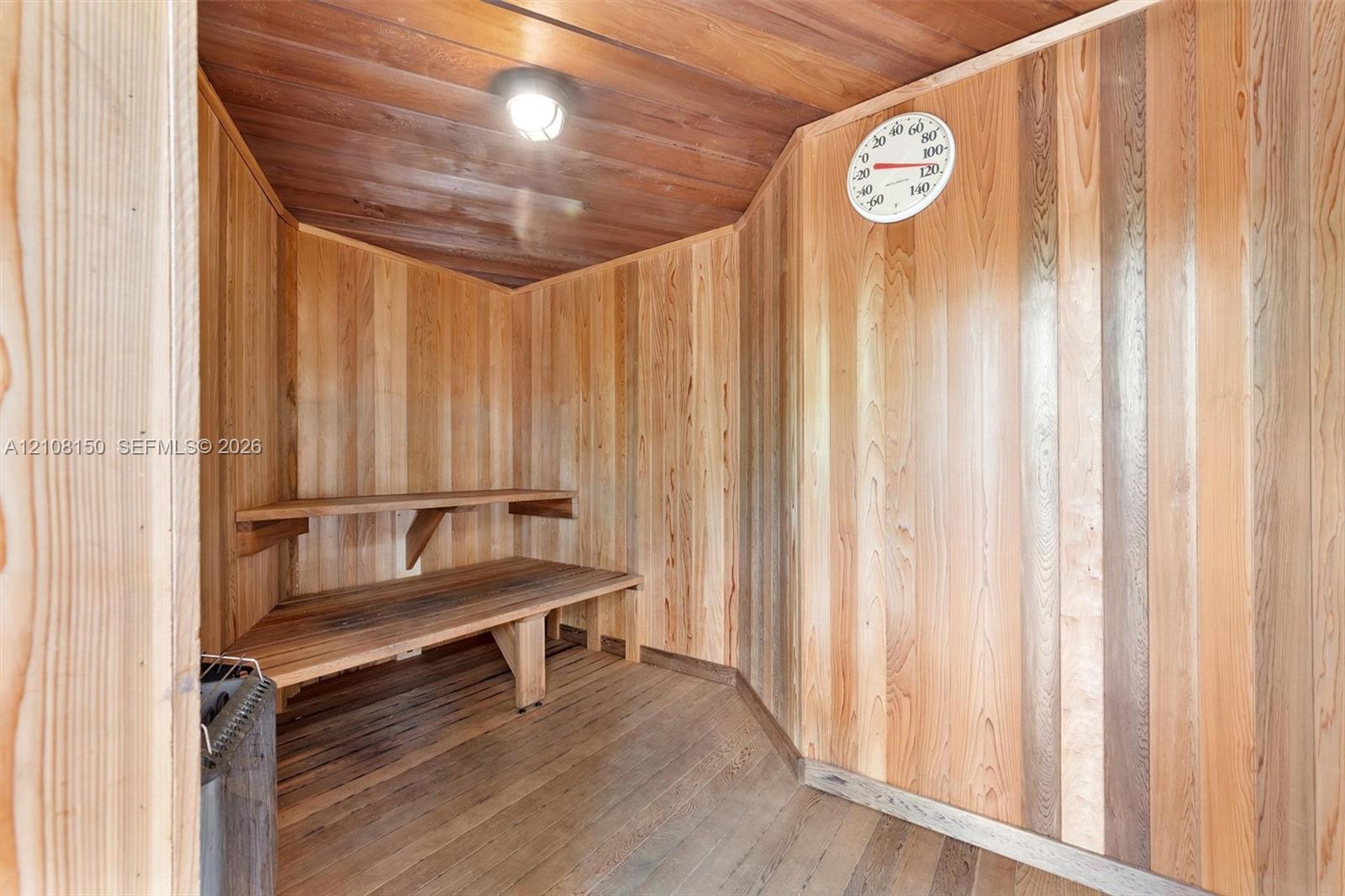 Sauna featuring wood paneling on walls and ceiling, tiered built-in wood benches, wall-mounted thermometer, and flush-mount lighting