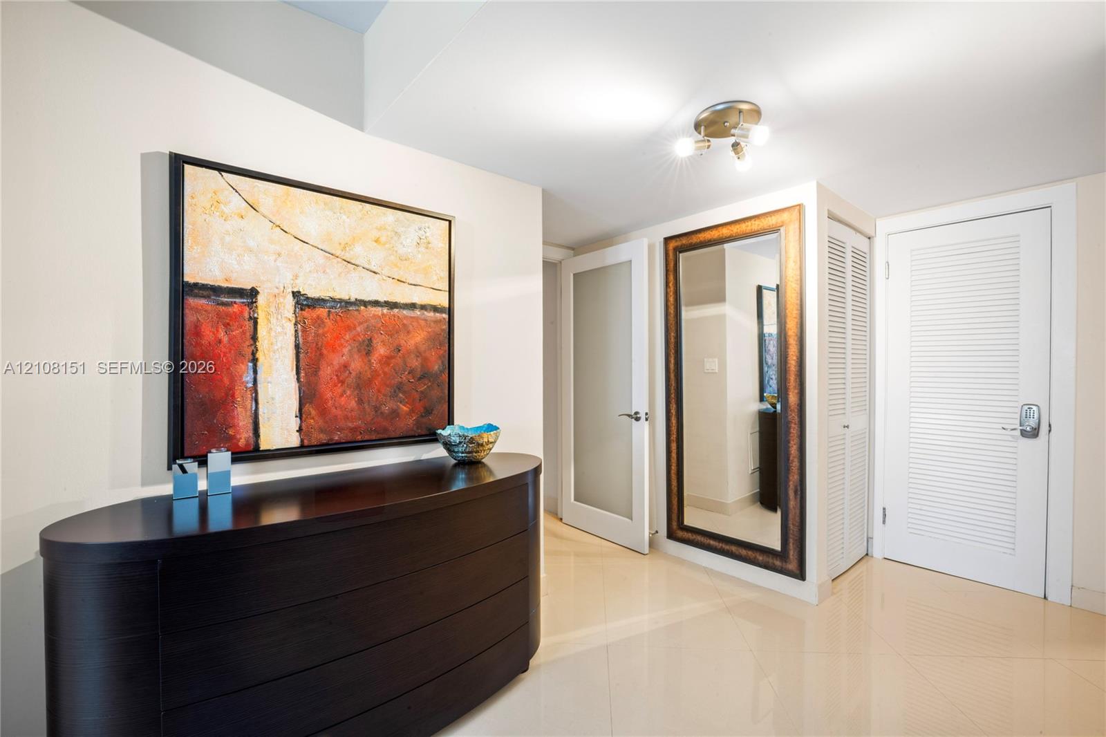 Entryway featuring large-format tile flooring, a frosted glass pane interior door, a louvered bi-fold closet, and a multi-bulb flush-mount ceiling fixture