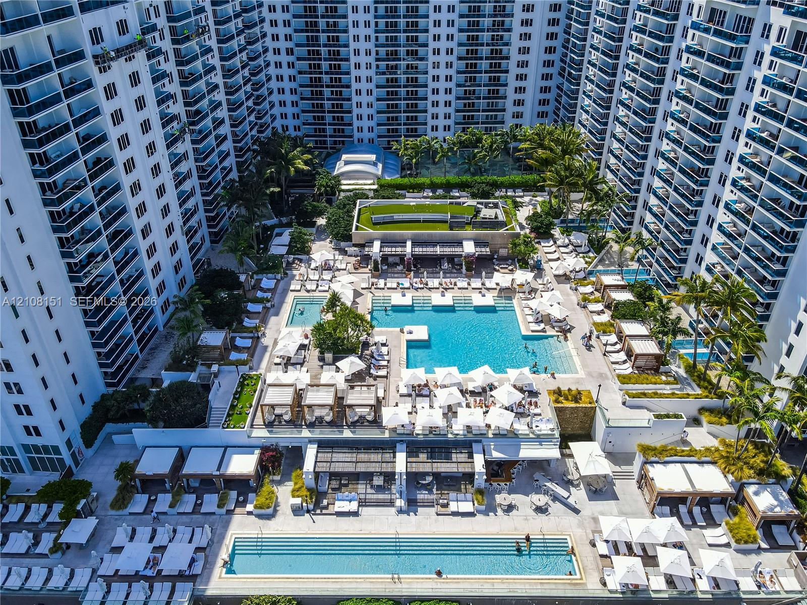 Aerial view of residential high-rise community featuring a sprawling multi-level pool deck, lap pool, cabanas, and manicured landscaping