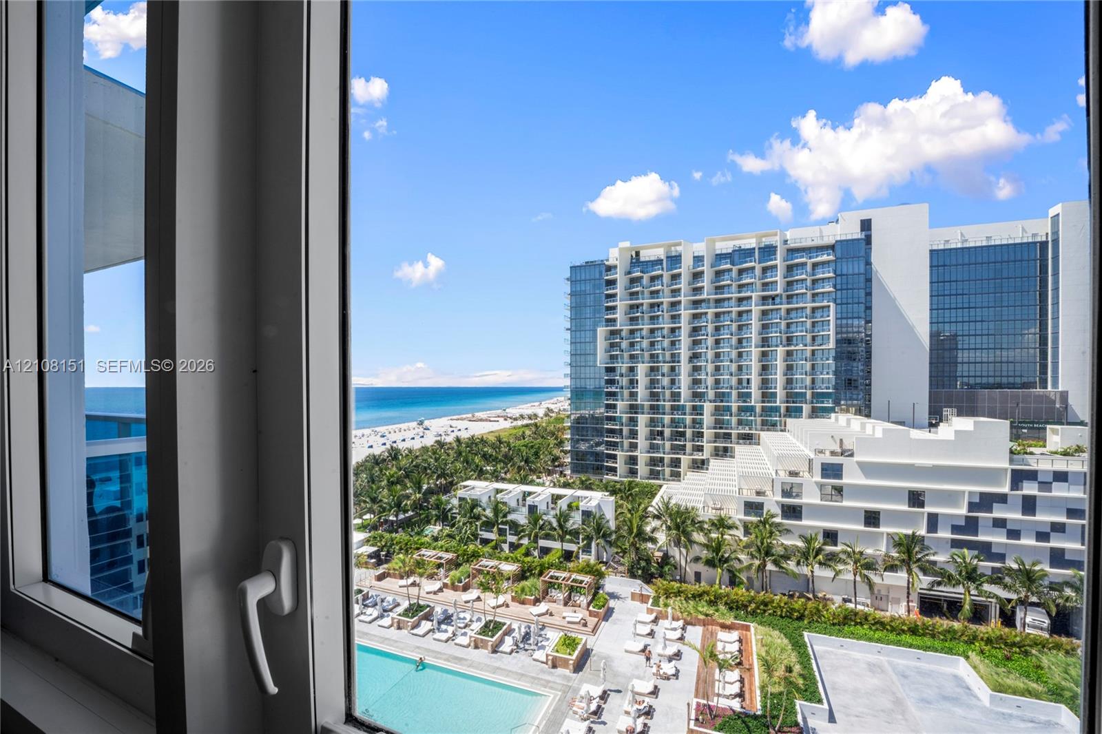 White-framed casement window overlooking a coastal horizon, featuring an exterior panorama of a multi-story glass facade building, tropical landscaping, and a swimming pool