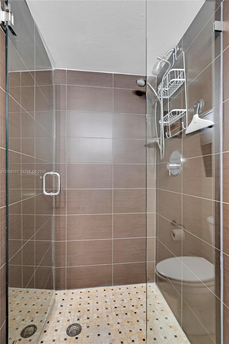 Walk-in shower featuring brown horizontal wall tile, a mosaic-tiled floor, a glass enclosure, and a chrome-finished shower system