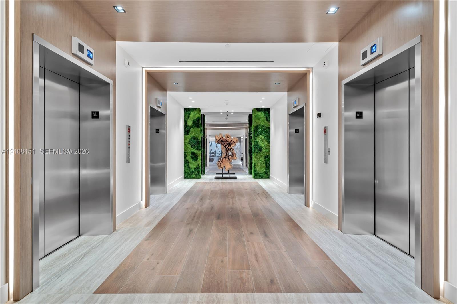 Elevator lobby featuring stainless steel doors, wood-finish wall paneling, integrated LED lighting, and decorative moss-covered columns