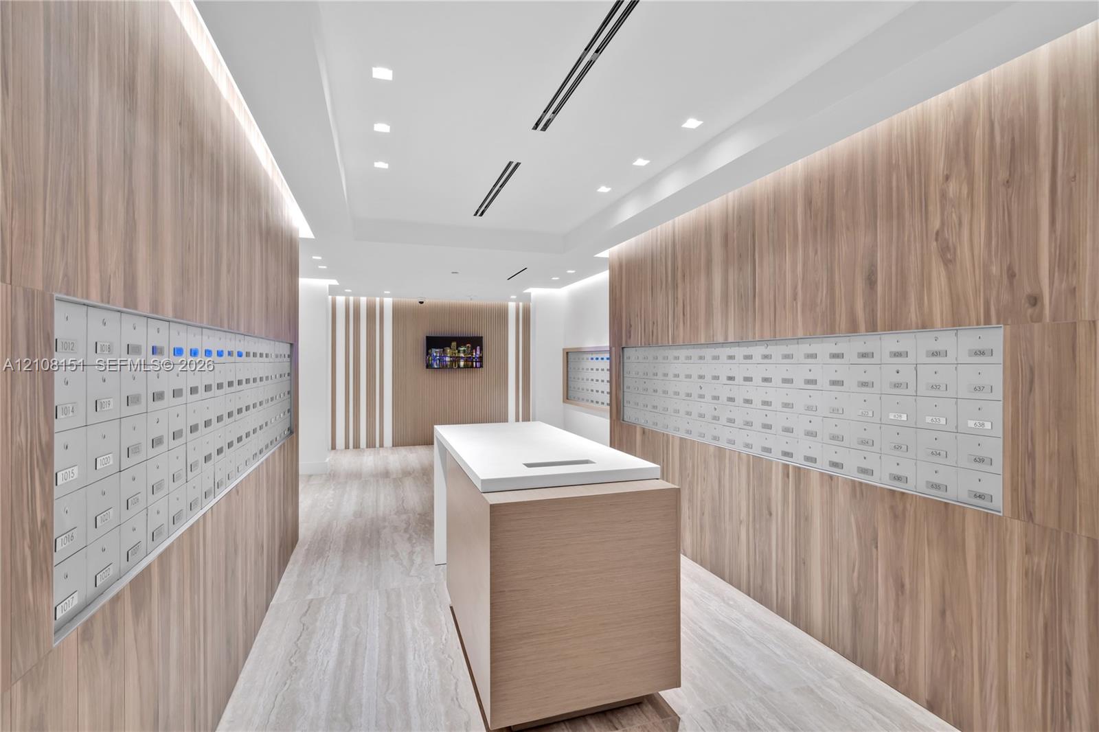 Modern lobby featuring wood-finish wall paneling, built-in parcel lockers, a central stone-topped island, recessed ceiling lighting, and wood-finish flooring