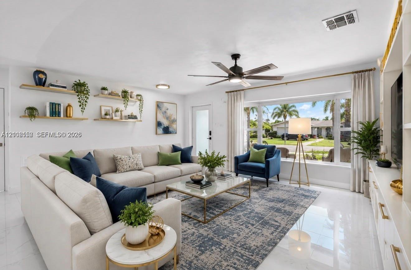Living area featuring a large bay window, light-toned tile flooring, custom built-in cabinetry, floating wall shelves, and a ceiling fan