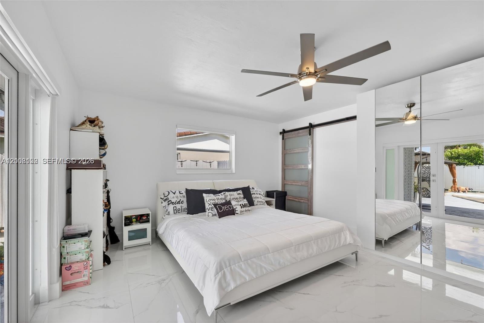 Polished tile flooring, mirrored closet doors, sliding barn-style door, and integrated ceiling fan with light fixture