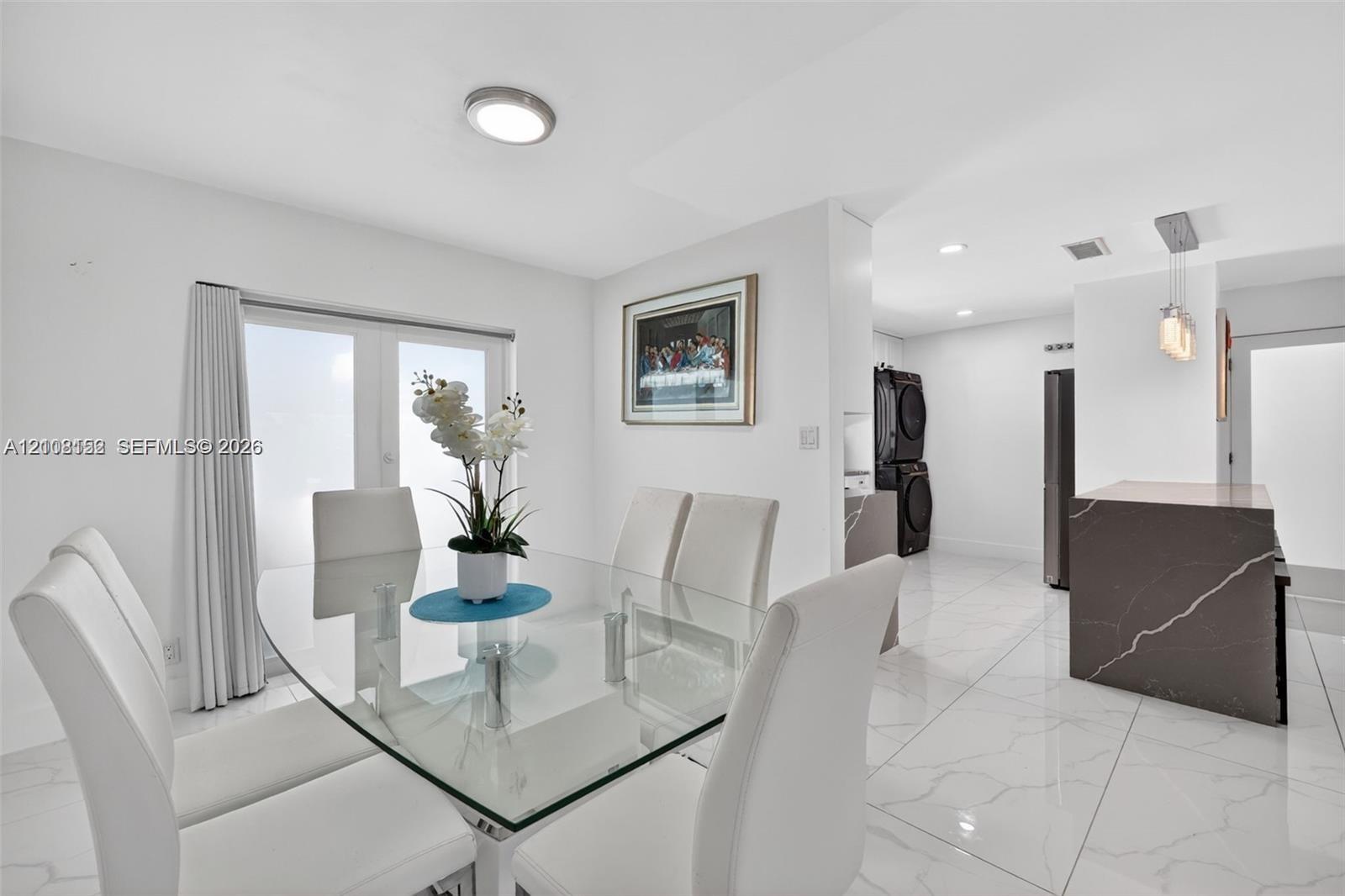 Large-format tile flooring, central recessed lighting, and kitchen island with waterfall-edge stone countertop