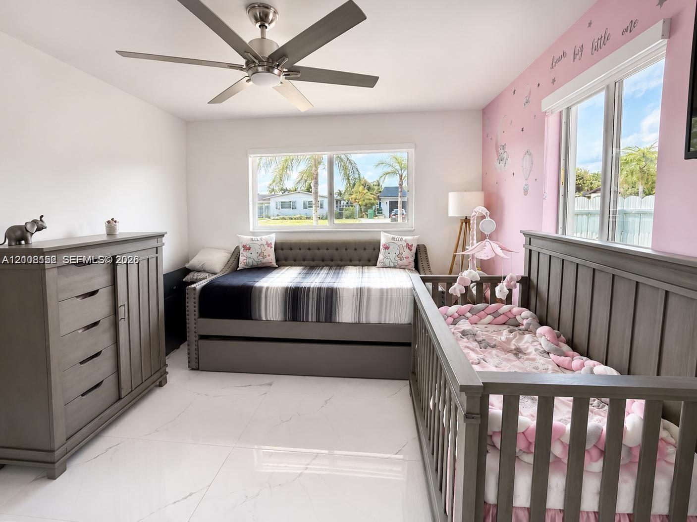 Bright room featuring large-format tile flooring, a brushed-nickel ceiling fan, and dual windows with natural light
