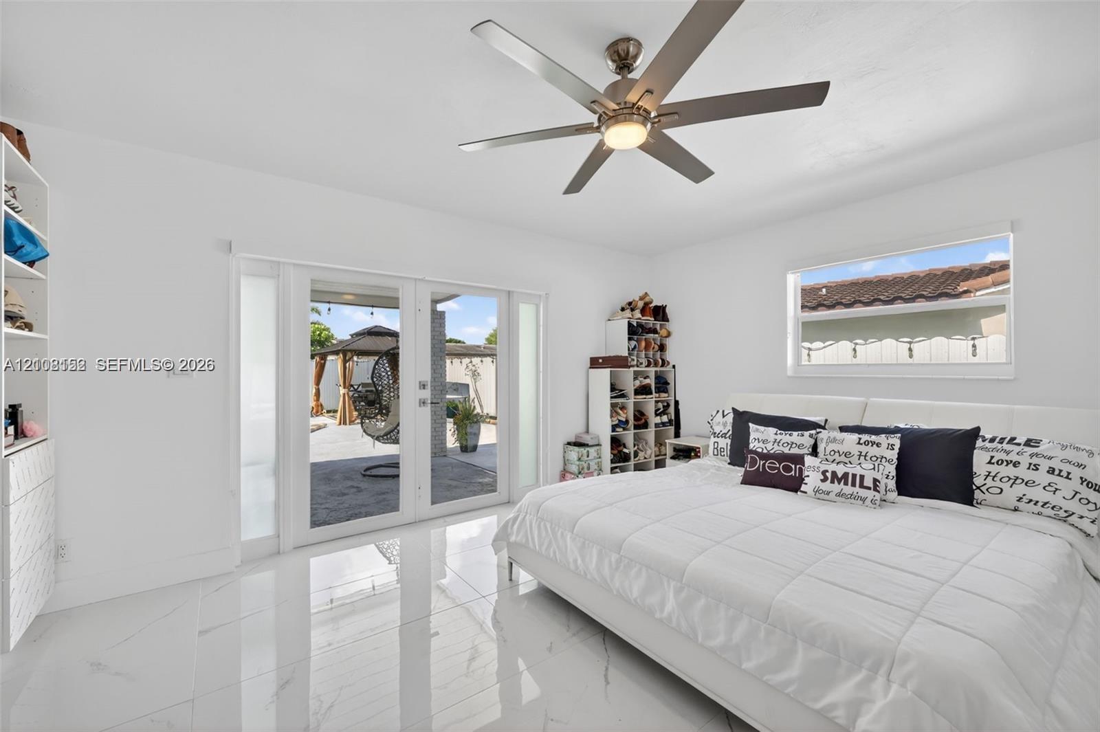 Glossy white tile flooring, ceiling fan with integrated lighting, built-in shelving, and dual glass-panel exterior doors