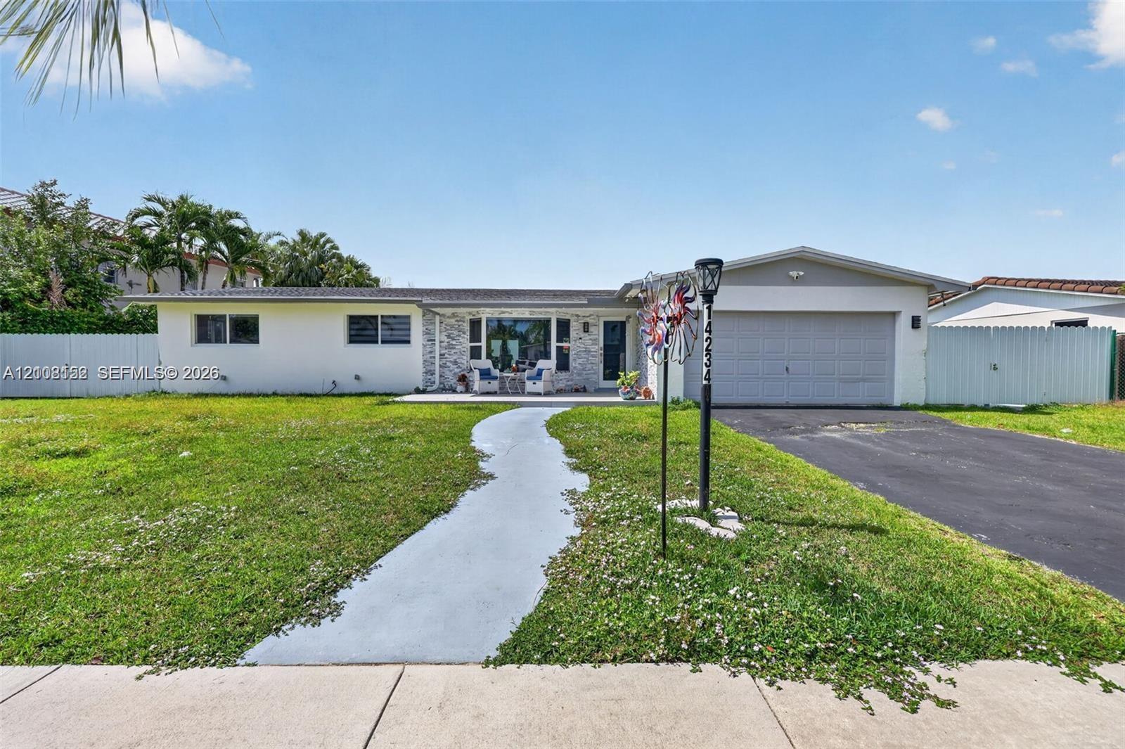 Single-story exterior featuring light-toned masonry accents, a paved front walkway, an attached two-car garage, and surrounding perimeter fencing
