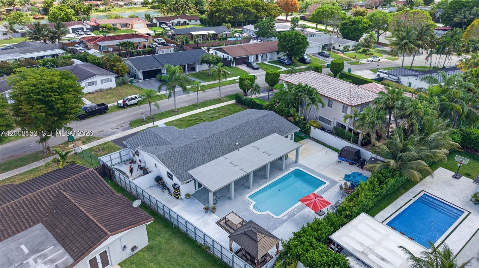 Aerial perspective featuring a single-story residence with a pitched shingle roof, an expansive covered patio, an in-ground swimming pool, and perimeter fencing