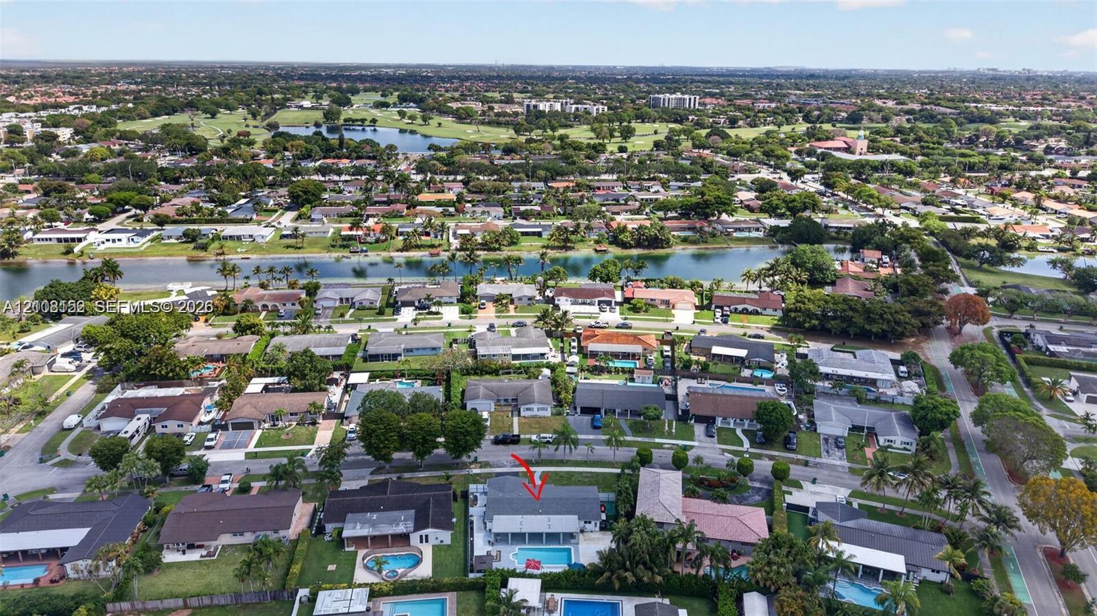 Aerial perspective of residential property featuring a private swimming pool, concrete patio, hipped roofline, and mature perimeter landscaping