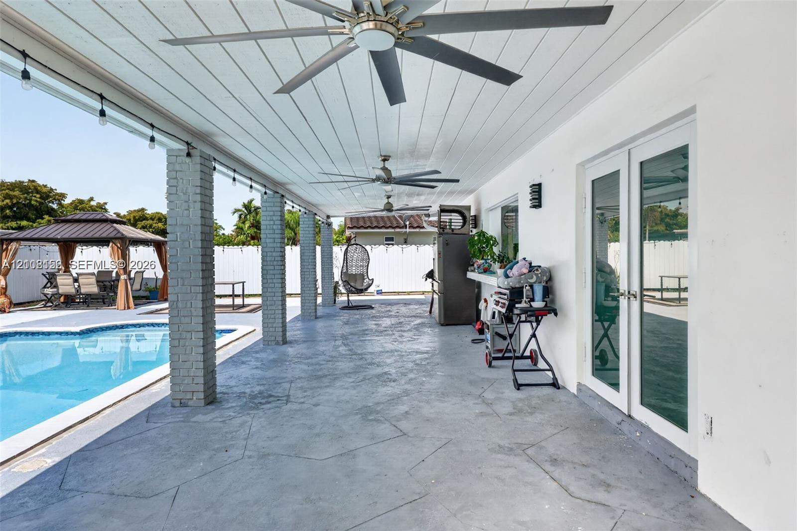 Covered patio featuring a stained concrete floor, tongue-and-groove plank ceiling, recessed ceiling fans, and brick support columns
