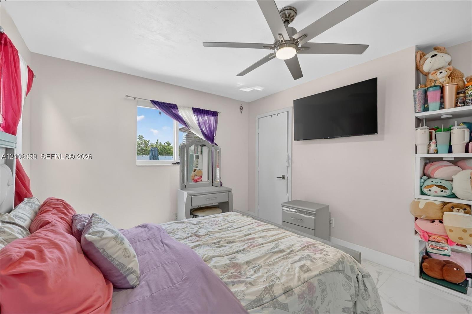 Neutral-toned room featuring a central ceiling fan with an integrated light fixture, light-colored tile flooring, and built-in shelving