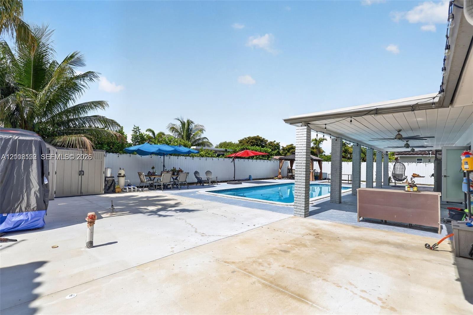 Outdoor living area featuring a covered patio with ceiling fans, an in-ground pool, expansive concrete hardscaping, and a white perimeter privacy fence