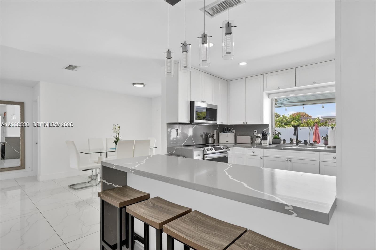 Kitchen featuring a waterfall-edge stone countertop, shaker-style cabinetry, stainless steel appliances, and multi-pendant lighting
