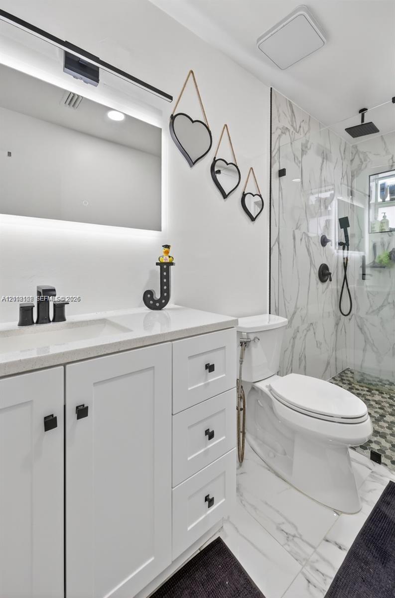 Bathroom featuring a white shaker-style vanity with stone-composite countertop, matte black hardware, integrated LED-backlit mirror, and glass-enclosed shower with large-format wall tile and geometric-patterned flooring
