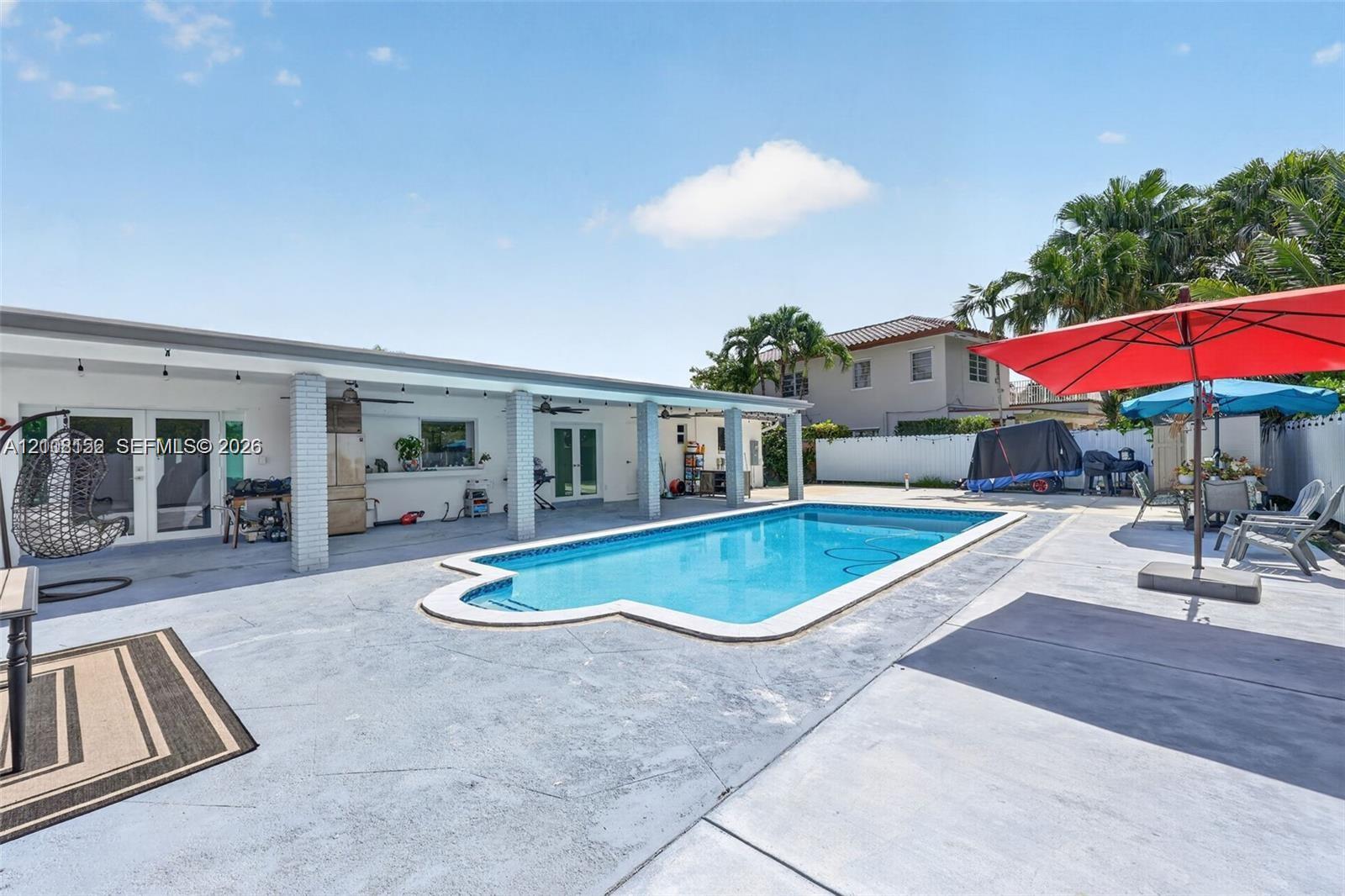 Swimming pool with perimeter coping, expansive concrete patio, and a covered terrace featuring structural columns
