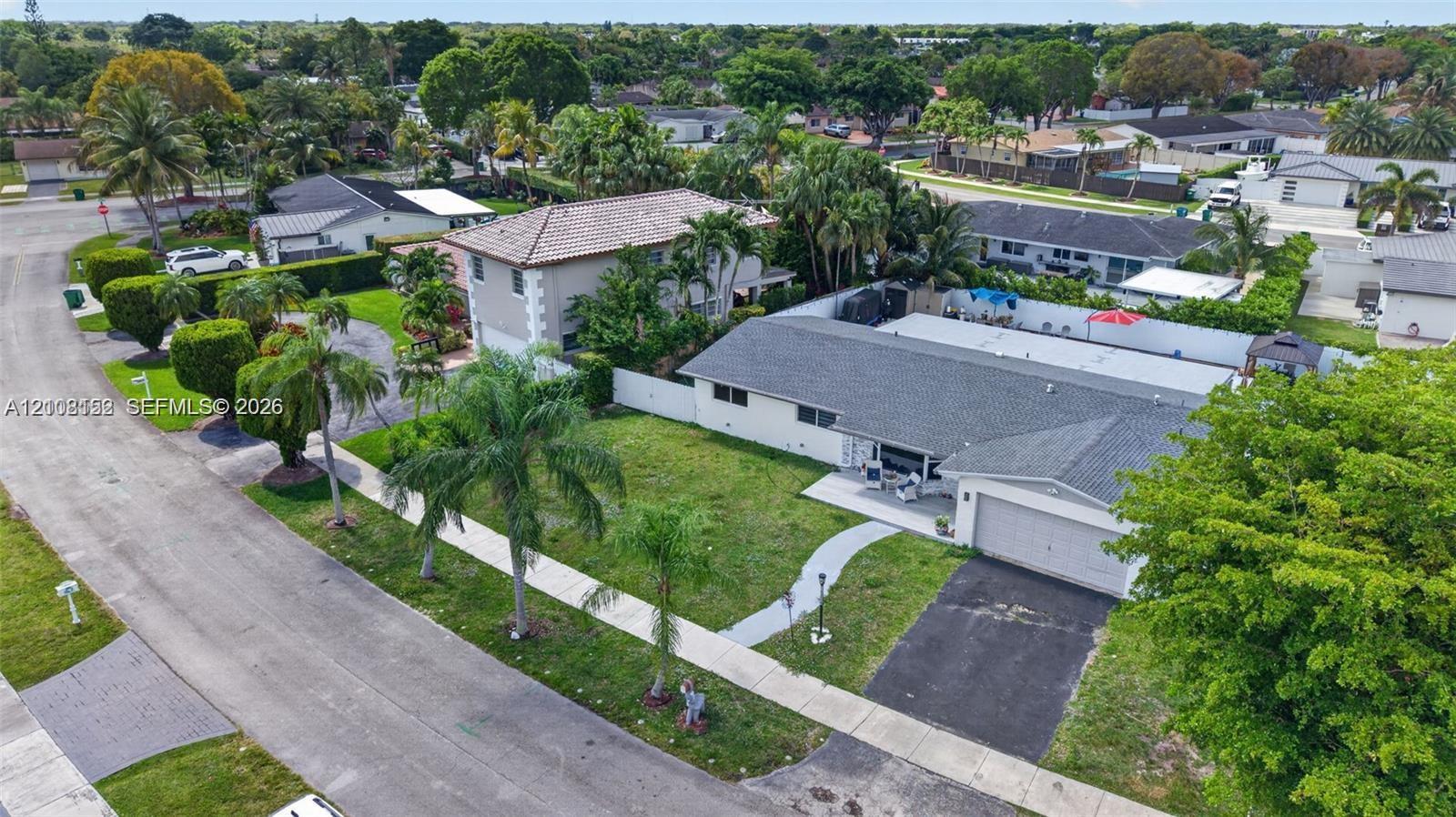 Aerial perspective of a residential property featuring an asphalt driveway, a single-car garage, a concrete walkway, and a perimeter privacy fence