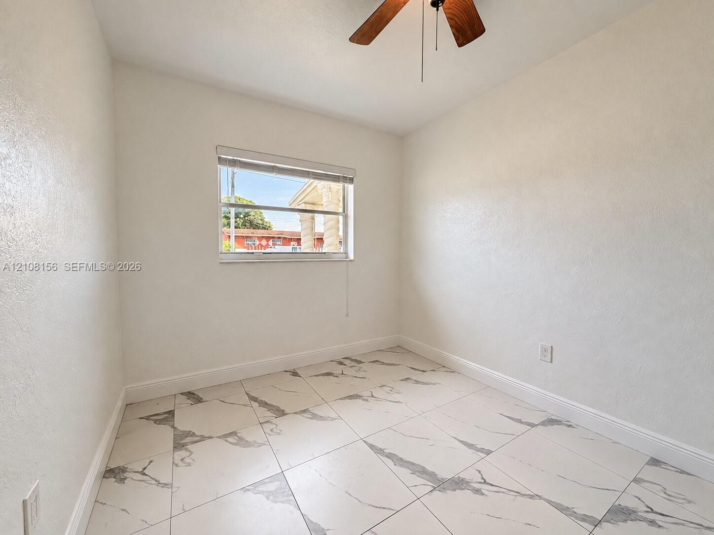 Room featuring large-format tile flooring with a neutral veined pattern, smooth wall finishes, a single-hung window, and a ceiling-mounted fan with wood-finish blades