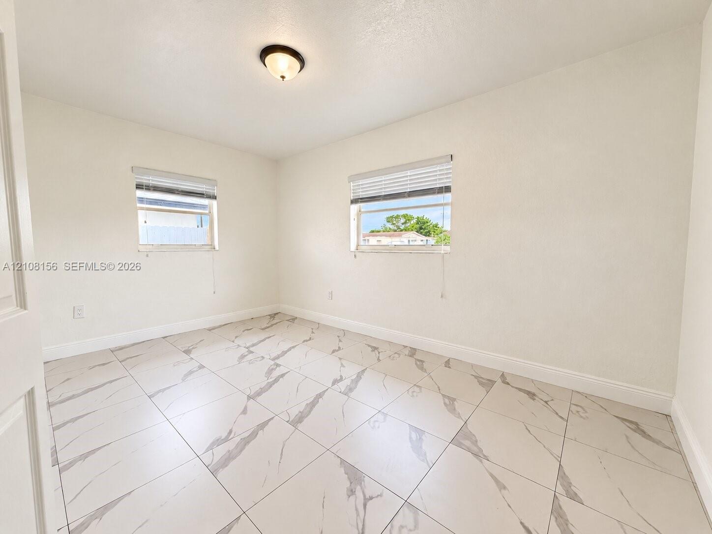 Room featuring large-format tile flooring with veining, two windows with horizontal blinds, and a centered flush-mount light fixture