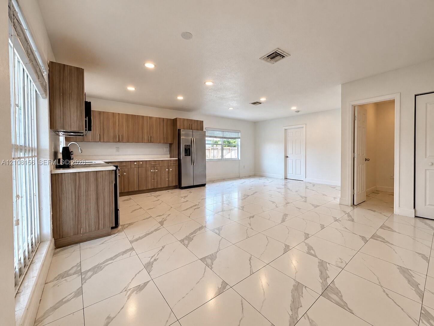Kitchen featuring wood-finish cabinetry, stainless steel refrigerator, white countertops, recessed lighting, and large-format porcelain tile flooring